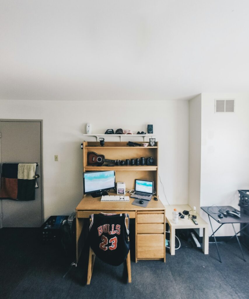 Small dorm-style room with a desk, computer and shelves