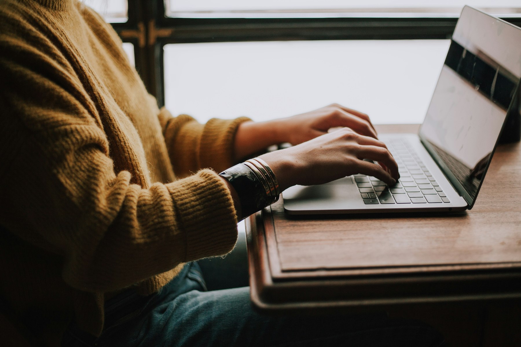 Person typing an email on a laptop at a desk by the window