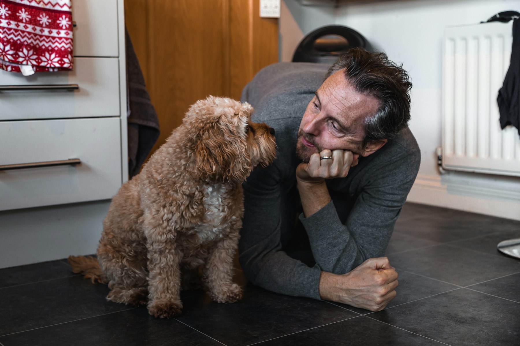 Man lying on the floor at home with his curly-haired dog beside him